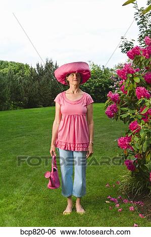 Stock Photograph - Woman in festive pink hat standing in garden. Fotosearch