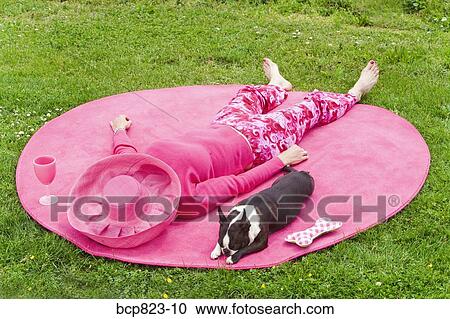 Stock Image - Woman in pink and dog relaxing outdoors on rug. Fotosearch