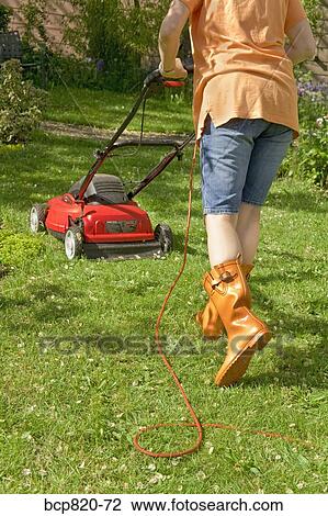 Stock Image - Woman mowing lawn with electric mower. Fotosearch