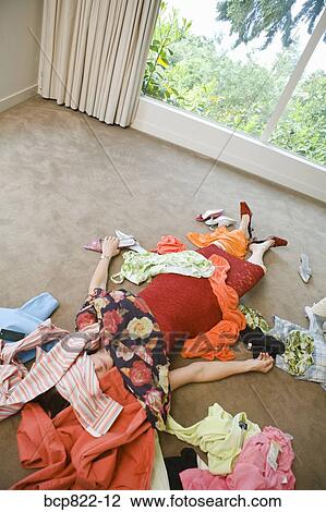 Stock Image - Woman on bedroom floor buried under clothing. Fotosearch
