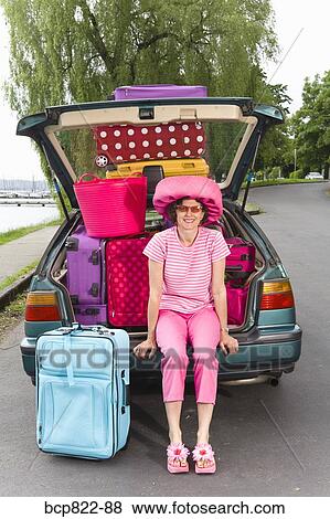Stock Photo - Woman posing with car loaded with colorful suitcases. Fotosearch