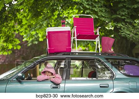 Stock Image - Woman sitting in car with picnic set on top. Fotosearch