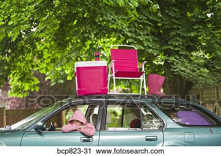 Stock Image - Woman sitting in car with picnic set on top. Fotosearch