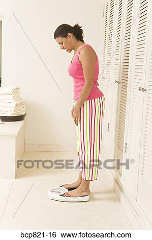 Stock Photograph - Woman standing on scale and wincing. Fotosearch