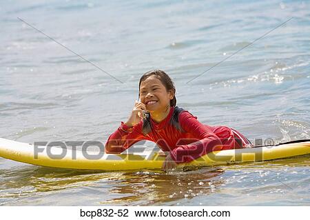 Stock Image - Girl lying on a surfboard and talking on a mobile phone. Fotosearch