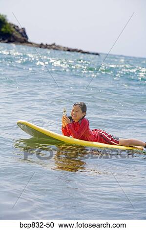 Girl lying on a surfboard and using a mobile phone View Large Photo Image Stock Image - Girl lying on a surfboard and using a mobile phone. Fotosearch