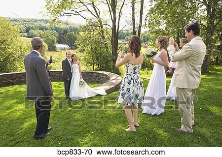 Stock Image - Group of people photographing a newlywed couple in a park, East Meredith, New York State, USA. Fotosearch