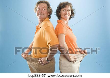 Stock Photo - Man and a woman wearing loose pants to show their weight loss. Fotosearch