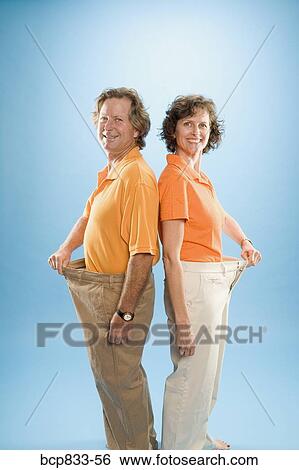 Man and a woman wearing loose pants to show their weight loss View Large Photo Image Stock Photograph - Man and a woman wearing loose pants to show their weight loss. Fotosearch