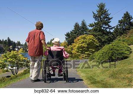 Picture - Man assisting his disabled mother in a wheelchair. Fotosearch