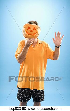 Stock Image - Man hiding his face with a Jack O' Lantern and waving his hand. Fotosearch