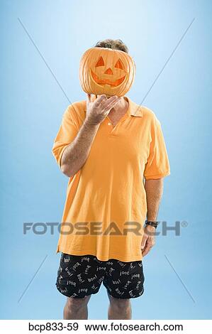 Stock Photo - Man hiding his face with a Jack O' Lantern. Fotosearch