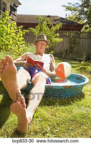 Stock Image - Man reading a book in a wading pool. Fotosearch