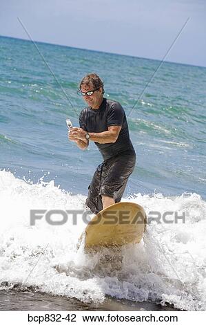 Man surfing in the sea and using a mobile phone View Large Photo Image Stock Image - Man surfing in the sea and using a mobile phone. Fotosearch