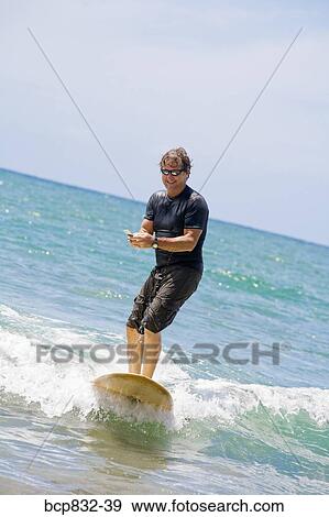 Man surfing in the sea and using a mobile phone View Large Photo Image Stock Photo - Man surfing in the sea and using a mobile phone. Fotosearch