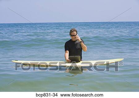 Picture - Man talking on a phone and using a laptop in the sea. Fotosearch