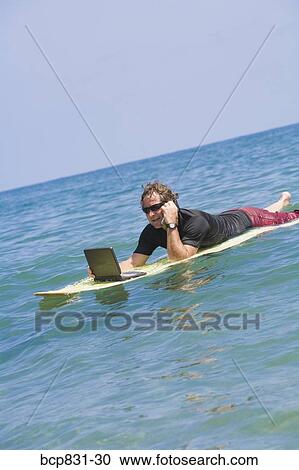 Stock Image - Man talking on a phone and using a laptop in the sea. Fotosearch