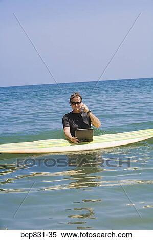 Stock Photography - Man talking on a phone and using a laptop in the sea. Fotosearch
