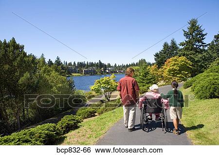 Stock Photograph - Man with a girl assisting a woman in a wheelchair. Fotosearch