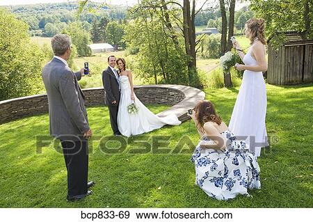 Stock Photo - Man with two women photographing a newlywed couple in a park, East Meredith, New York State, USA. Fotosearch