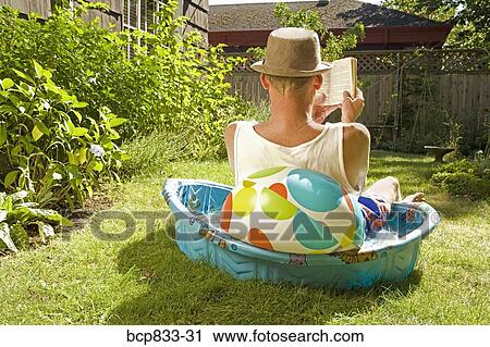 Rear view of a man reading a book in a wading pool View Large Photo Image Stock Image - Rear view of a man reading a book in a wading pool. Fotosearch