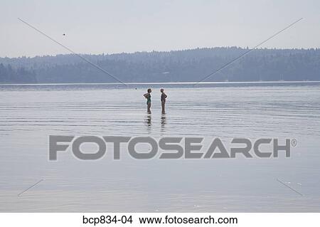Picture - Two women standing in the sea with arms akimbo, Washington State, USA. Fotosearch