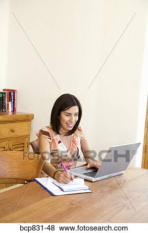 Woman sitting in front of a laptop and writing on a notebook View Large Photo Image Stock Photo - Woman sitting in front of a laptop and writing on a notebook. Fotosearch