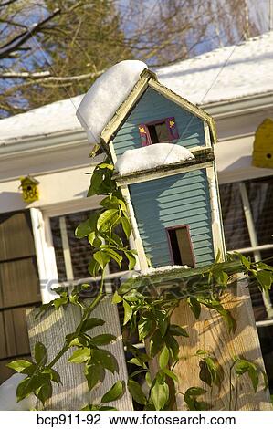 Stock Image - Bird house perched on a fence during winter. Fotosearch