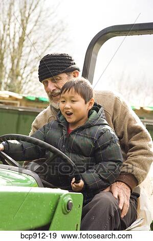 Stock Photo - Boy driving a tractor with assistance of male adult. Fotosearch