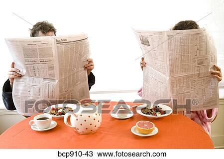 Stock Image - Couple having breakfast and reading newspaper together. Fotosearch