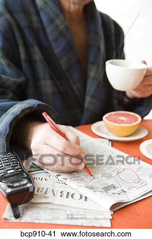 Stock Image - Man having tea and researching classifieds. Fotosearch
