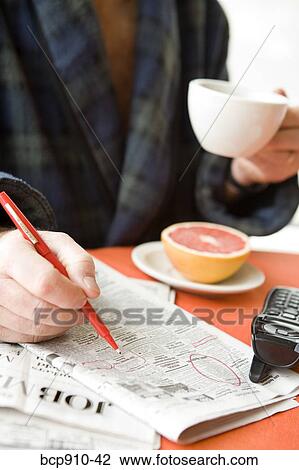 Stock Image - Man having tea and researching classifieds. Fotosearch