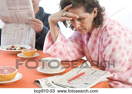 Stock Image - Tired woman with her husband at breakfast looking at classifieds. Fotosearch