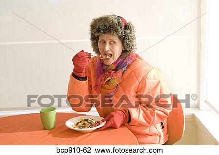 Stock Image - Woman dressed in winter apparel eating breakfast. Fotosearch