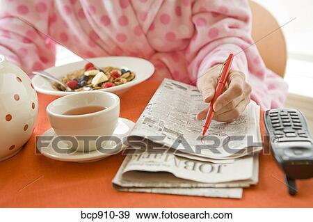 Stock Photo - Woman having breakfast and researching classifieds. Fotosearch