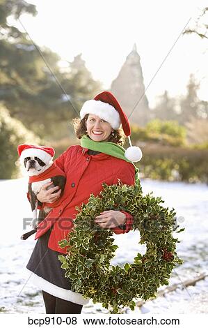 Woman in a park holding a Christmas wreath and a dog View Large Photo Image Stock Photo - Woman in a park holding a Christmas wreath and a dog. Fotosearch