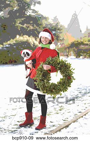 Woman in a park holding a Christmas wreath and a dog View Large Photo Image Stock Photo - Woman in a park holding a Christmas wreath and a dog. Fotosearch