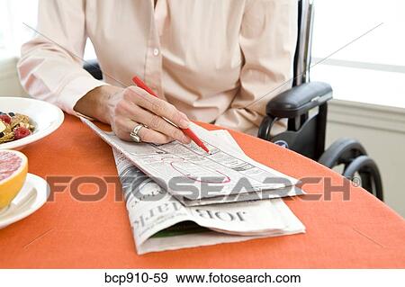Stock Photo - Woman in a wheelchair at breakfast searching classifieds. Fotosearch