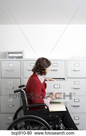 Stock Image - Woman in a wheelchair opening drawer on file cabinet. Fotosearch