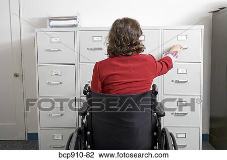 Stock Image - Woman in a wheelchair opening drawer on file cabinet. Fotosearch