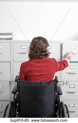 Stock Image - Woman in a wheelchair opening drawer on file cabinet. Fotosearch