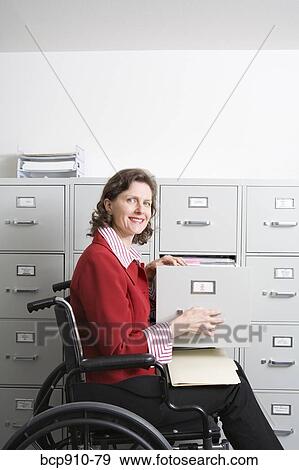 Woman in a wheelchair opening drawer on file cabinet View Large Photo Image Stock Photo - Woman in a wheelchair opening drawer on file cabinet. Fotosearch