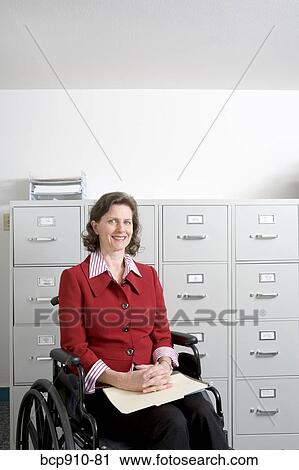 Stock Image - Woman in wheelchair in front of file cabinet. Fotosearch