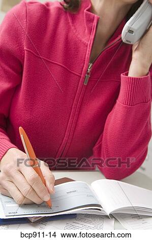 Picture - Woman writing a check while talking on phone. Fotosearch