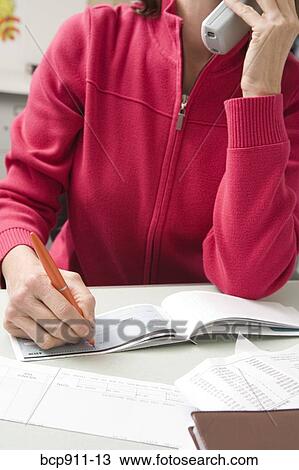Woman writing a check while talking on phone View Large Photo Image Stock Image - Woman writing a check while talking on phone. Fotosearch
