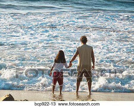 Stock Image - Man and girl looking at surf. Fotosearch