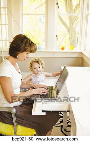 Stock Image - Woman with young child in home office. Fotosearch
