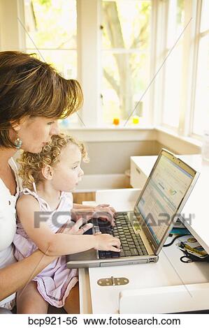Stock Photograph - Woman with young child in home office. Fotosearch