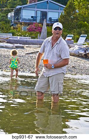 Stock Photo - angry man standing in water with cocktail. Fotosearch
