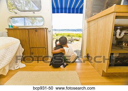 Stock Image - Boy and dog sitting in camper doorway. Fotosearch